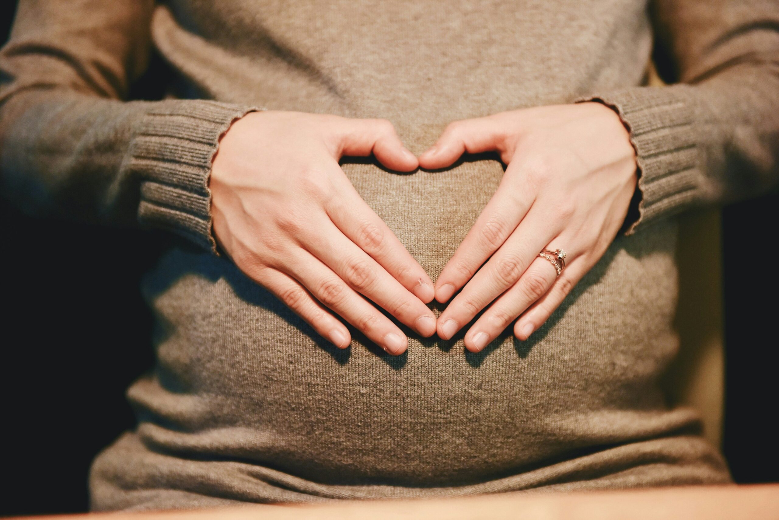 Woman in a jersey using her hands to form the shape of a heart over her pregnancy bump